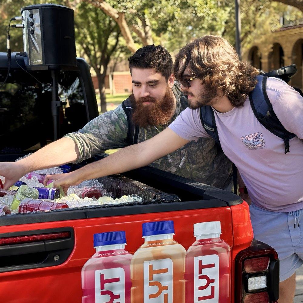 Two students reach into an iced pickup truck bed full of sports drinks during a campus sampling stop
