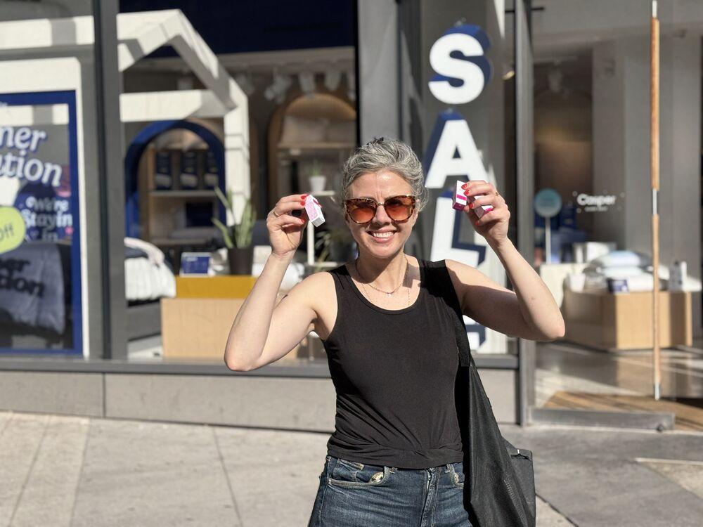An ambassador in sunglasses holds up two pink sample boxes outside a storefront