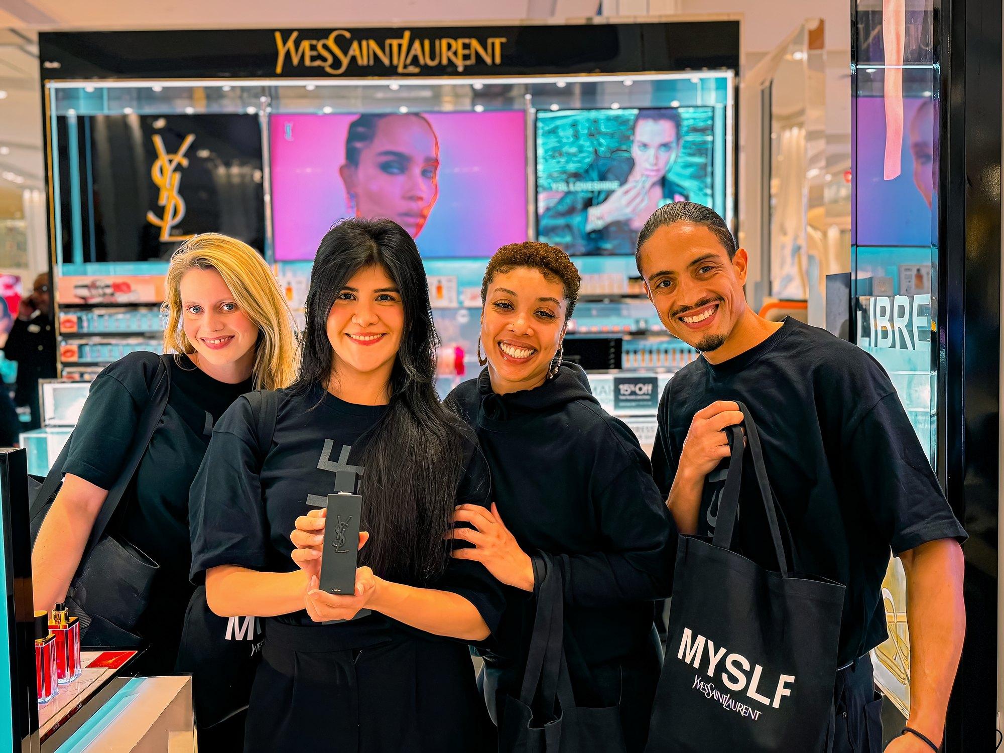 Four ambassadors smile at a luxury beauty counter in a department store, one holding a fragrance bottle