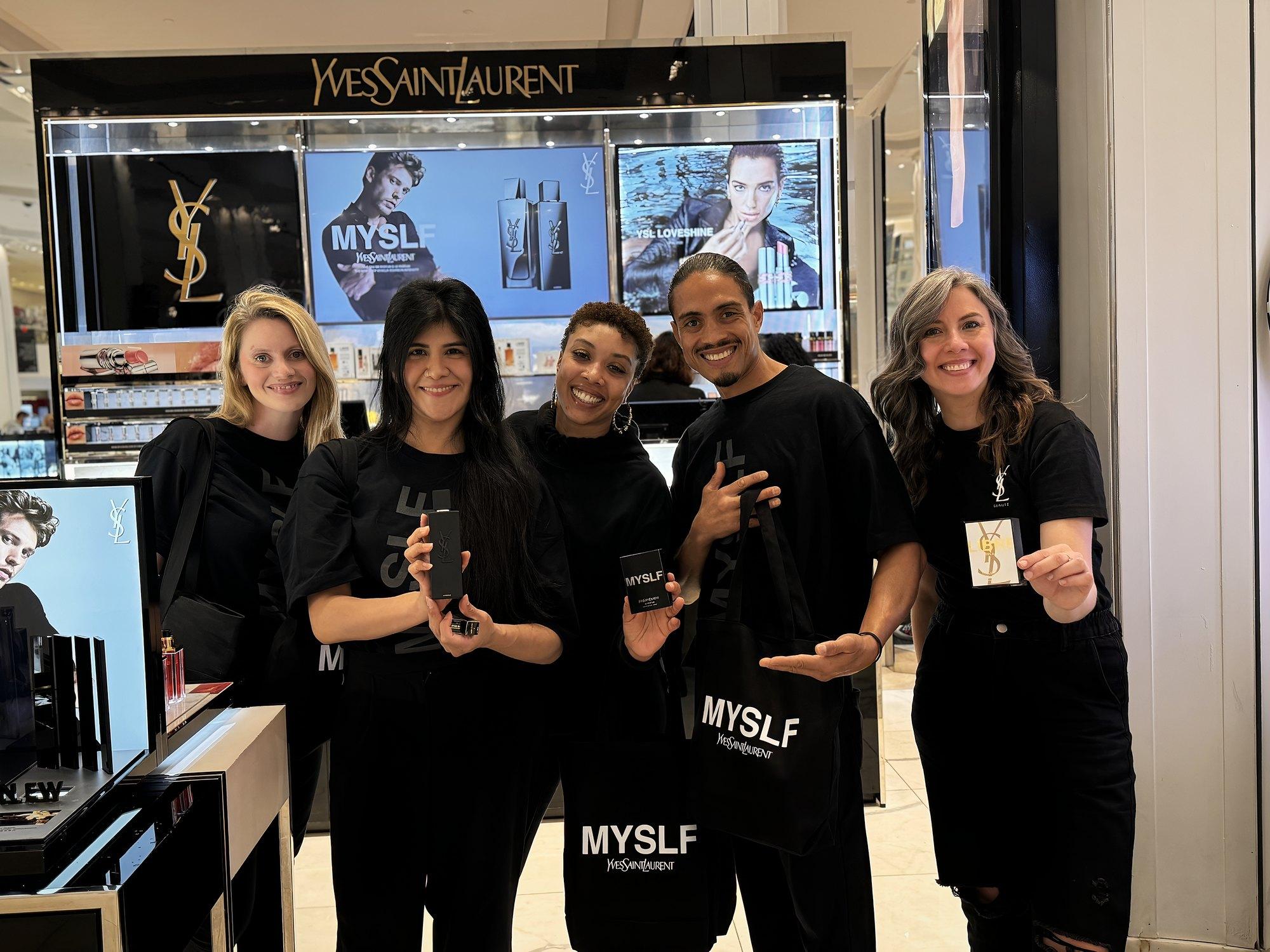 Five-person fragrance launch team at a department store beauty counter, holding samples and tote bags